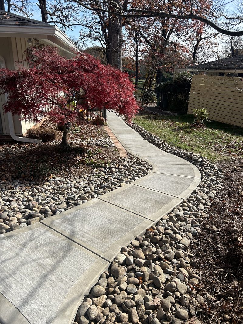 Curved broom finish concrete sidewalk with river rock landscaping in residential yard in Spartanburg SC